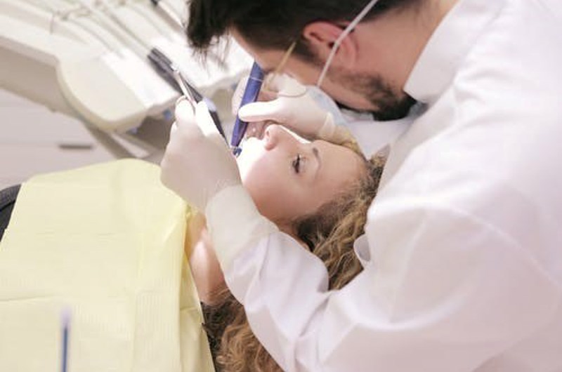 Billedet viser en tandlæge der arbejder på en patient.